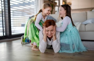 A happy mother having fun with little daughters in princess costumes at home.