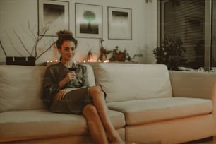 Uma jovem feliz sentada no sofá e bebendo vinho à noite.