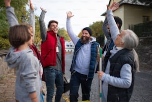 A diverse group of happy community service volunteers raising hands together outdoors in street