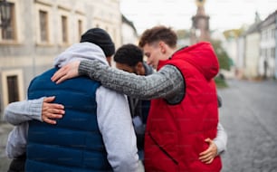 A rear view of community service volunteers hugging together outdoors in street