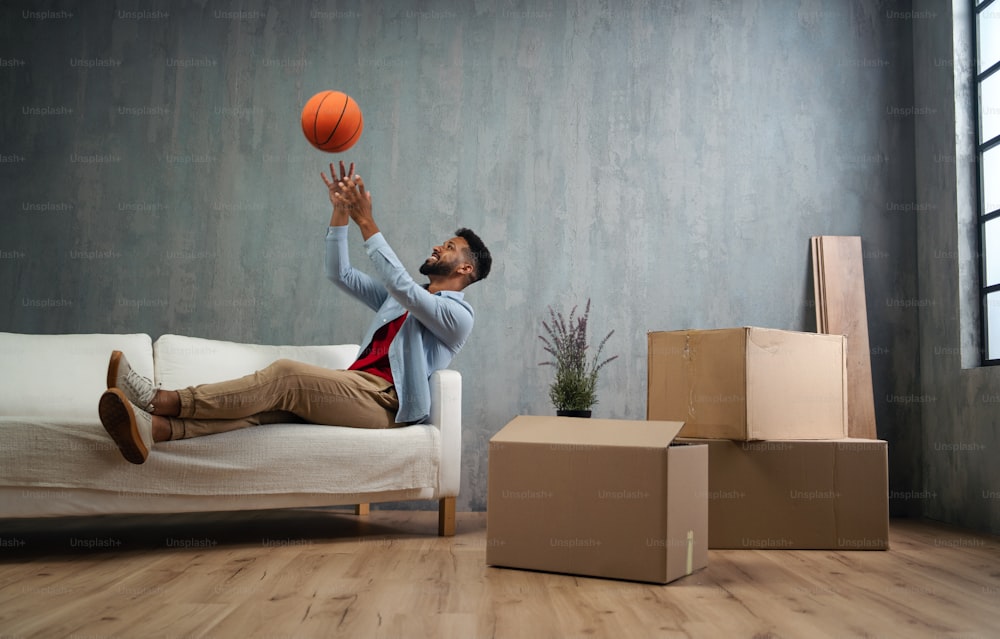 Um jovem feliz com basquete comemorando a mudança para casa cercado por caixas de embalagem, novo conceito de vida.