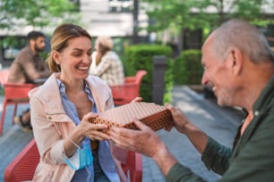 Ein älterer Vater, der einer erwachsenen Tochter im Freien in der Stadt ein Geschenk macht und sich in einem Café-Konzept trifft.