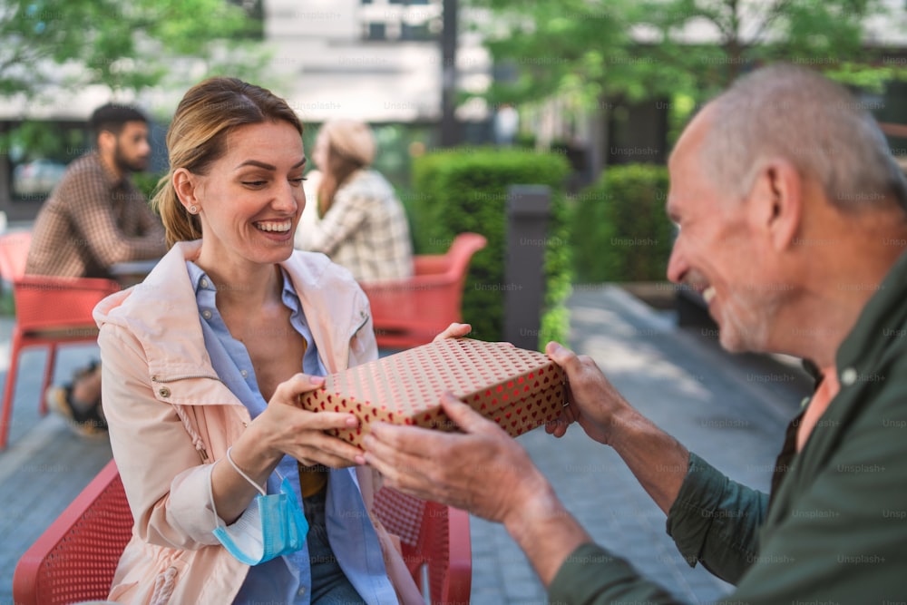 Un padre mayor dando un regalo a un adulto al aire libre en la ciudad, reuniéndose en un concepto de café.