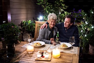 車椅子の幸せな老夫婦が夕方にテラスで夕食をとり、楽しい時間を過ごす。