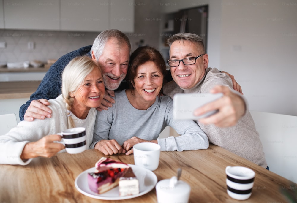 Groupe d’amis seniors joyeux à la maison, prenant selfie avec smartphone.
