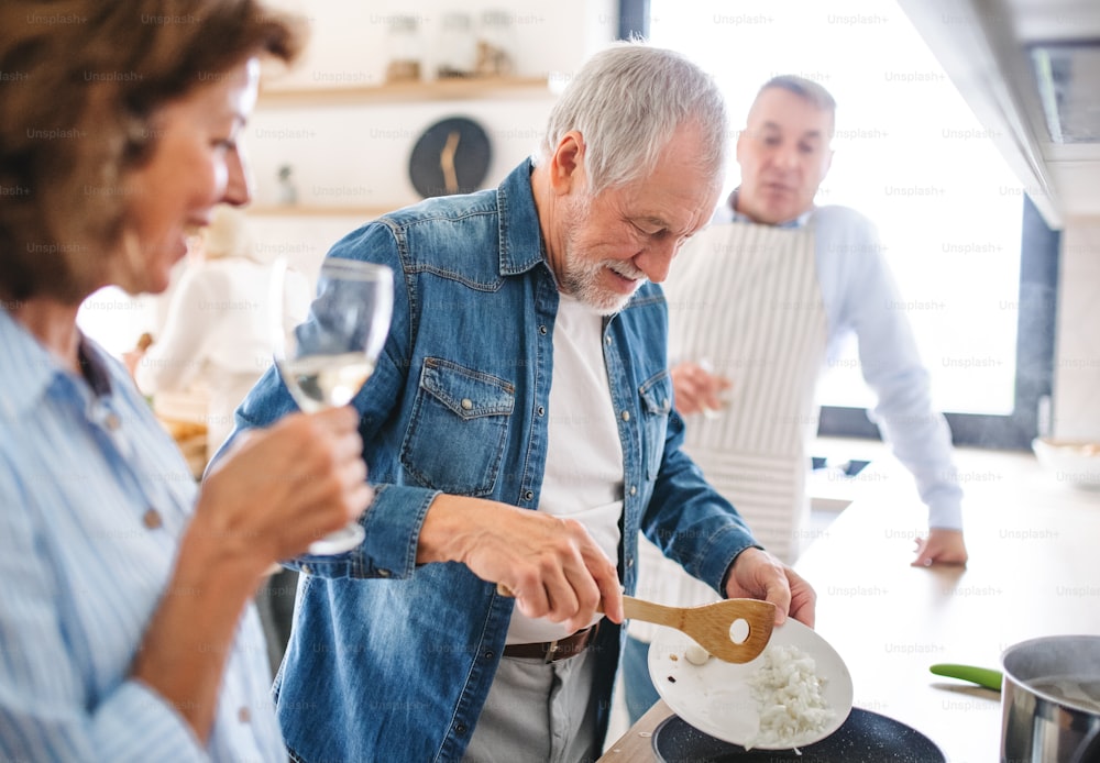 Vista frontal do grupo de amigos idosos alegres no jantar em casa, cozinhando.