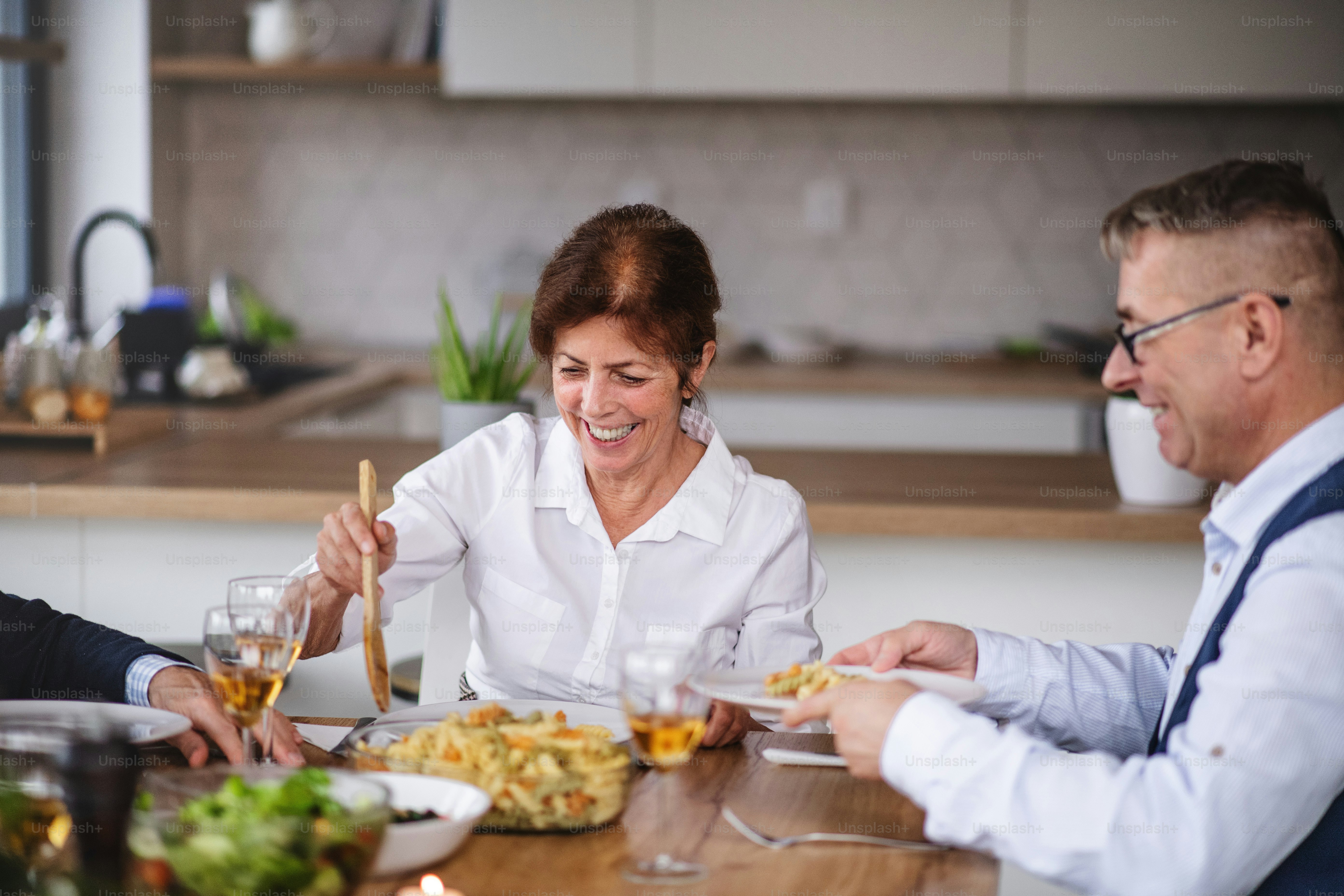 Gruppo di amici anziani che si godono la cena a casa, mangiando.