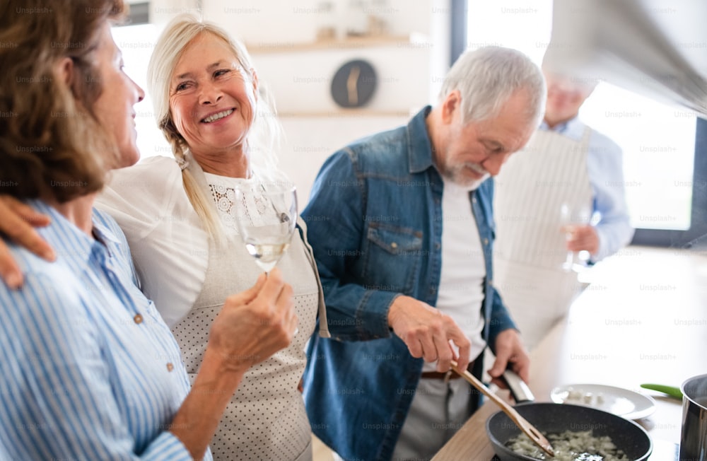 Vista frontal do grupo de amigos idosos alegres no jantar em casa, cozinhando.
