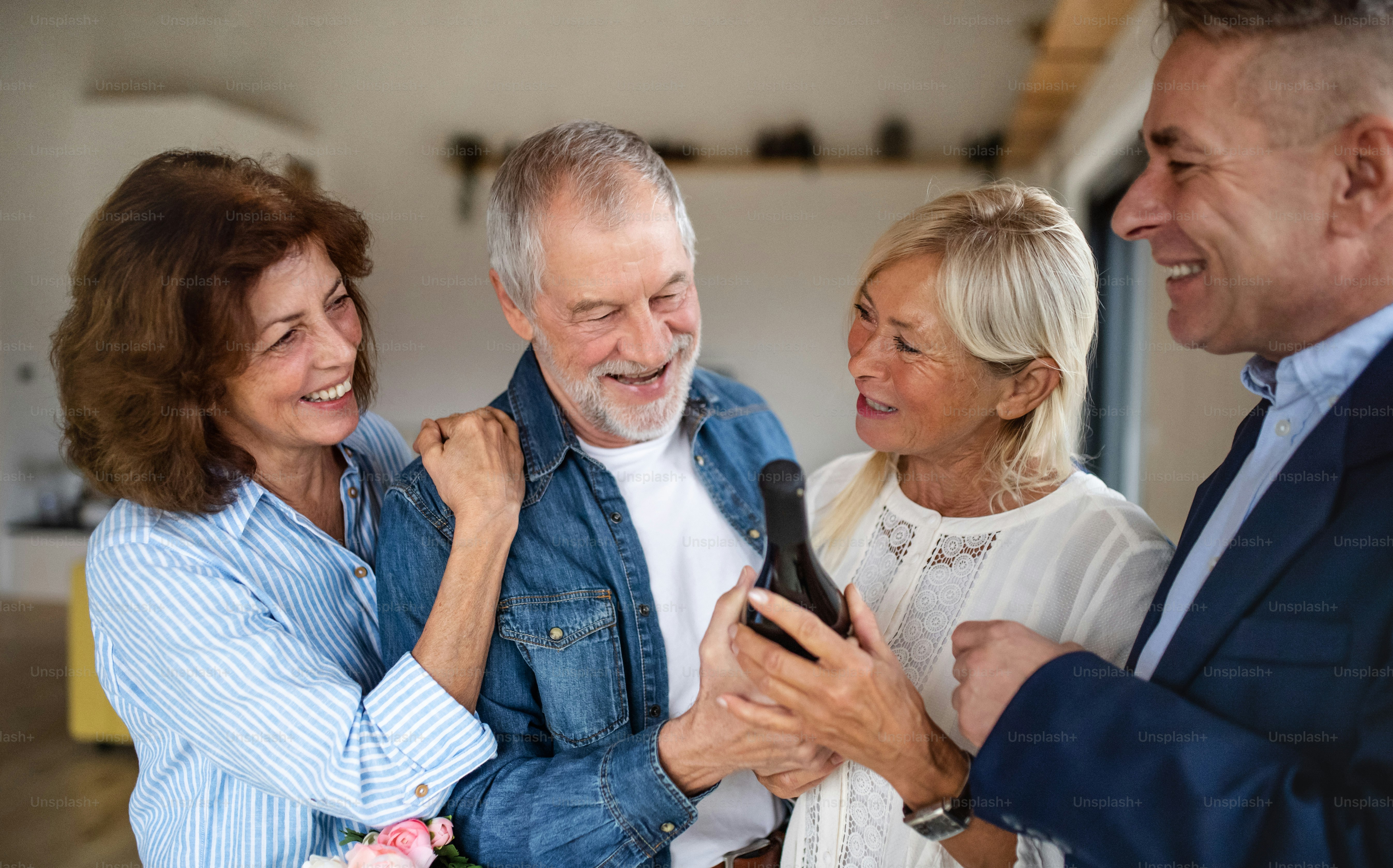 A group of cheerful senior friends at dinner party at home, greeting ...