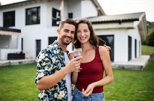 Front view portrait of young couple with wine outdoors in backyard, looking at camera.