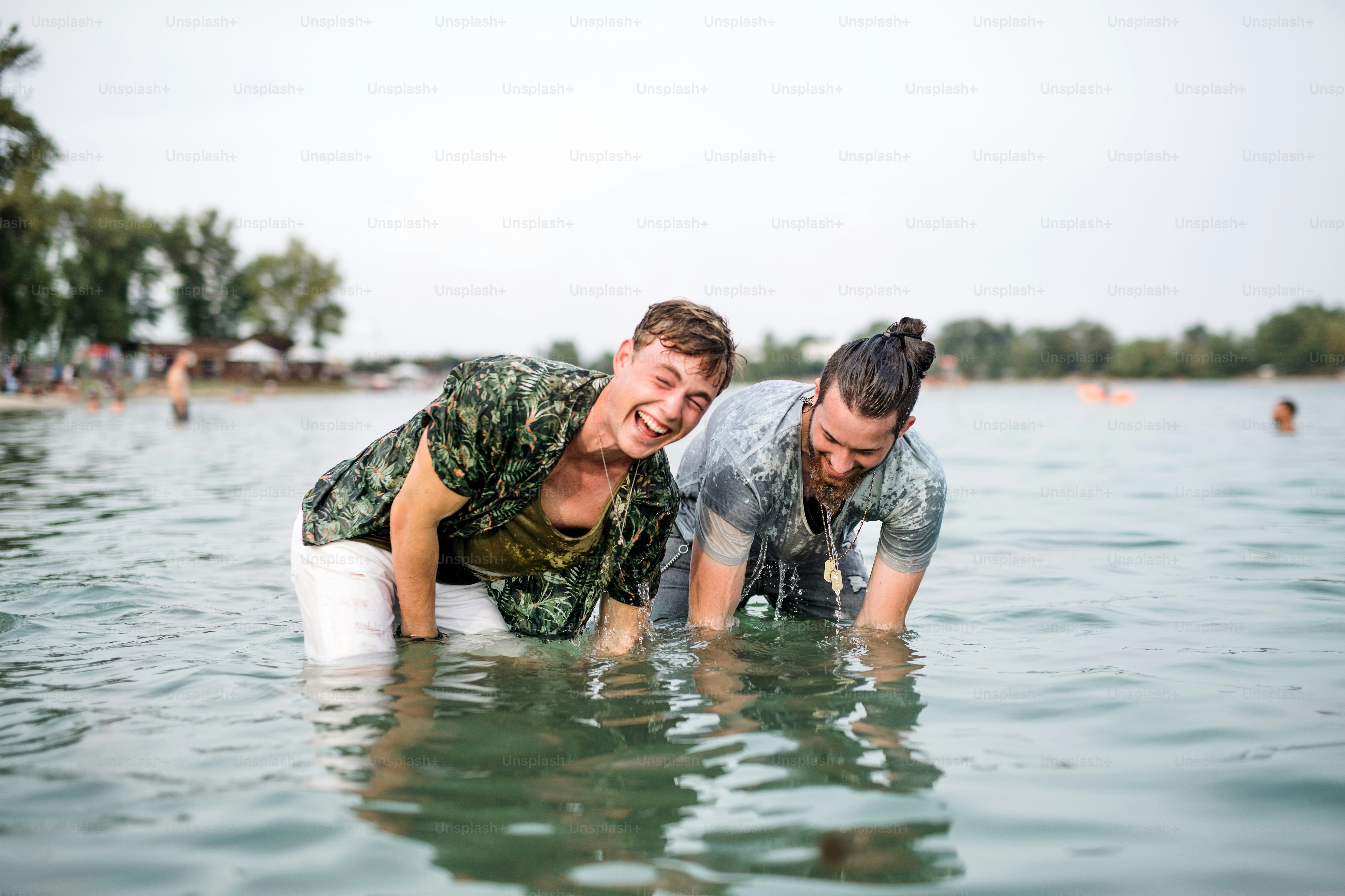 Wet young men friends at summer festival, standing in lake and looking at camera.