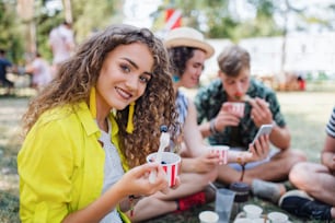 Hermosa joven con amigos sentada en el suelo en el festival de verano, comiendo fruta.