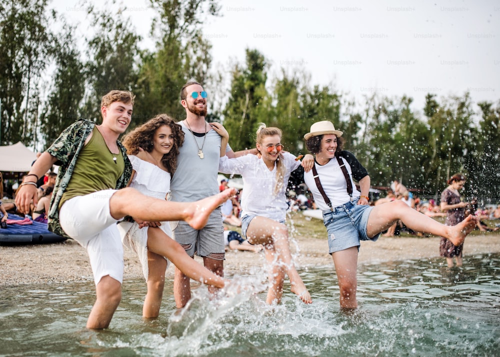 Grupo de jóvenes amigos en el festival de verano, de pie en el lago y salpicando agua.
