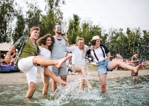 Group of young friends at summer festival, standing in lake and splashing water.