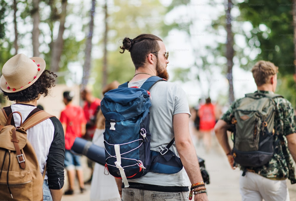 Vue arrière d’un groupe de jeunes amis au festival d’été ou vacances en camping, à pied.
