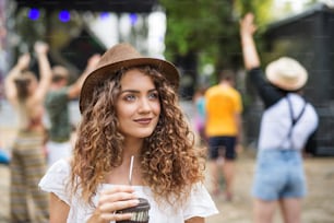 Vista frontal de una hermosa joven en el festival de verano, con bebida.