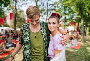 Front view portrait of young couple at summer festival, walking arm in arm.