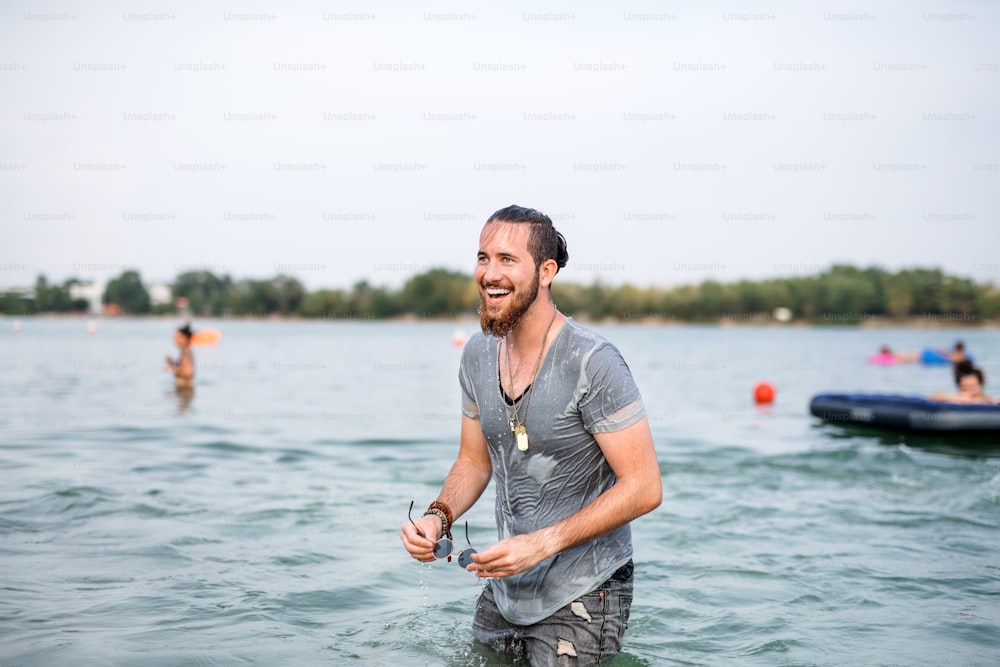 Young wet man having fun at summer festival, standing in lake. Copy space.