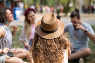 Group of cheerful young friends sitting on ground at summer festival, talking.