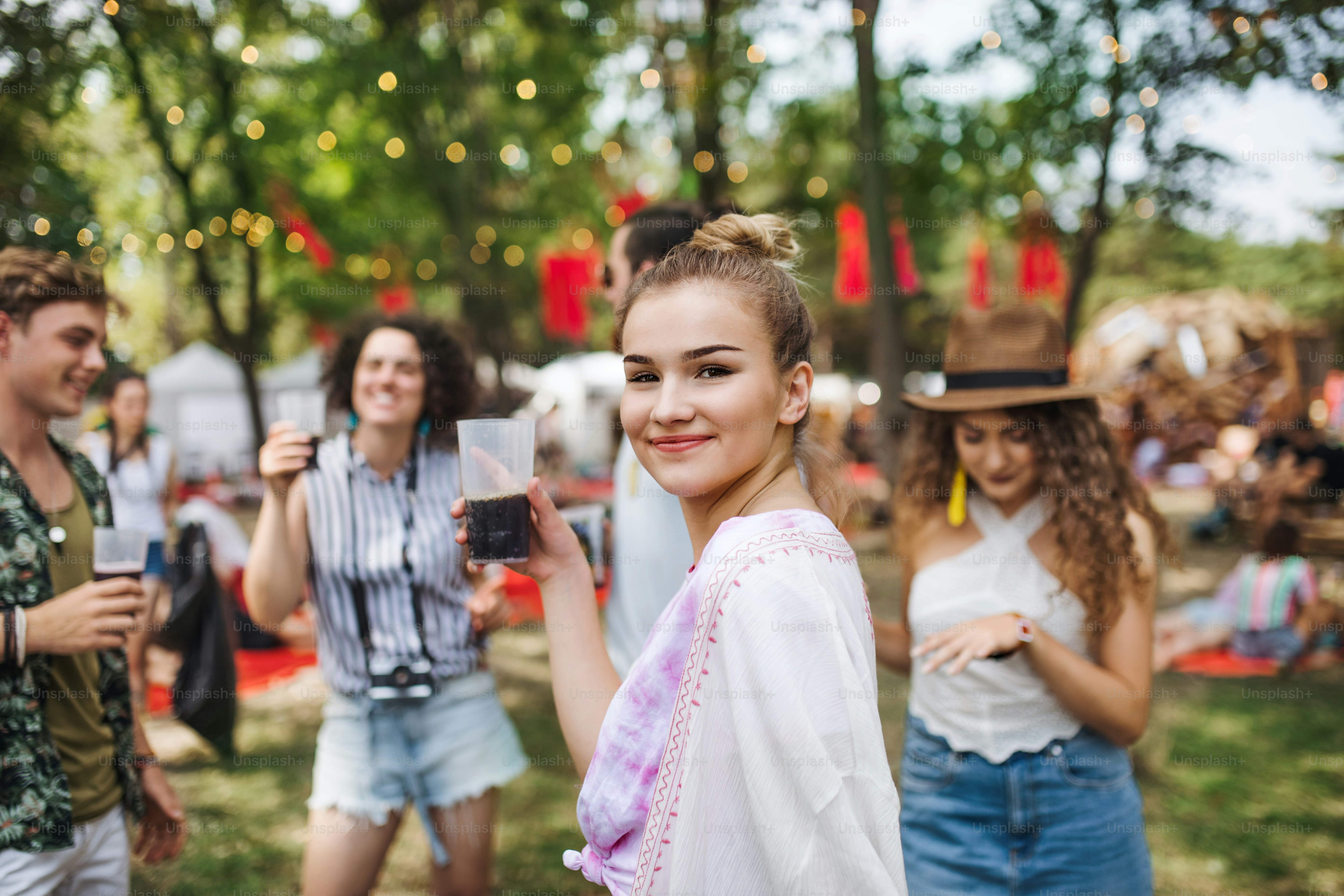 Un grupo de jóvenes amigos con bebidas en el festival de verano, de pie y hablando