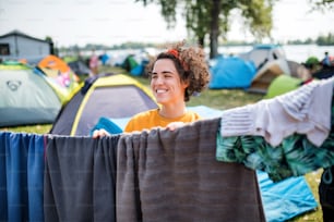 Front view of young woman hanging towels at summer festival or camping holiday.