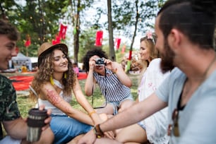Gruppo di giovani amici seduti a terra al festival estivo, scattando foto con la macchina fotografica.