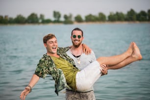 Fröhliche junge Männerfreunde, die sich beim Sommerfest amüsieren und im See stehen.