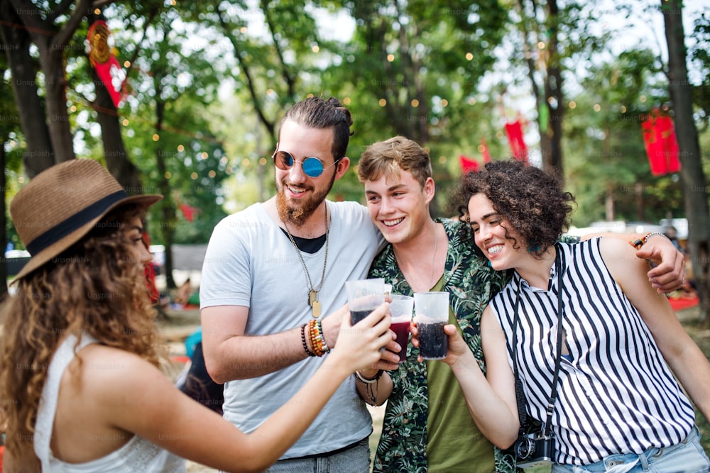 Un grupo de jóvenes amigos con bebidas en el festival de verano, de pie.
