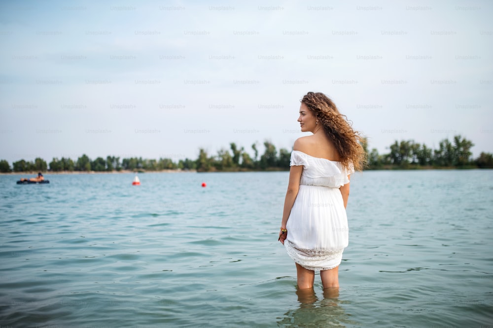 Rear view of young woman at summer festival, standing in lake. Copy space.