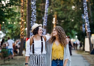 Portrait of two cheerful young women friends at summer festival, walking.