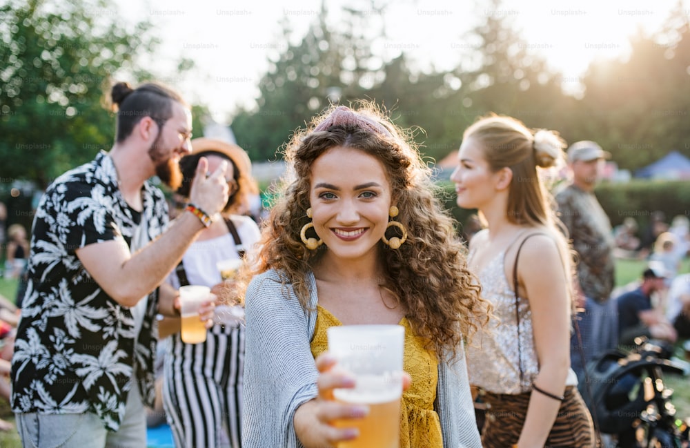 A group of young friends with drinks at summer festival, standing and talking.