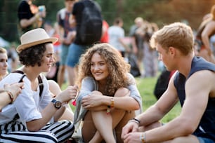 Group of cheerful young friends sitting on ground at summer festival, talking.