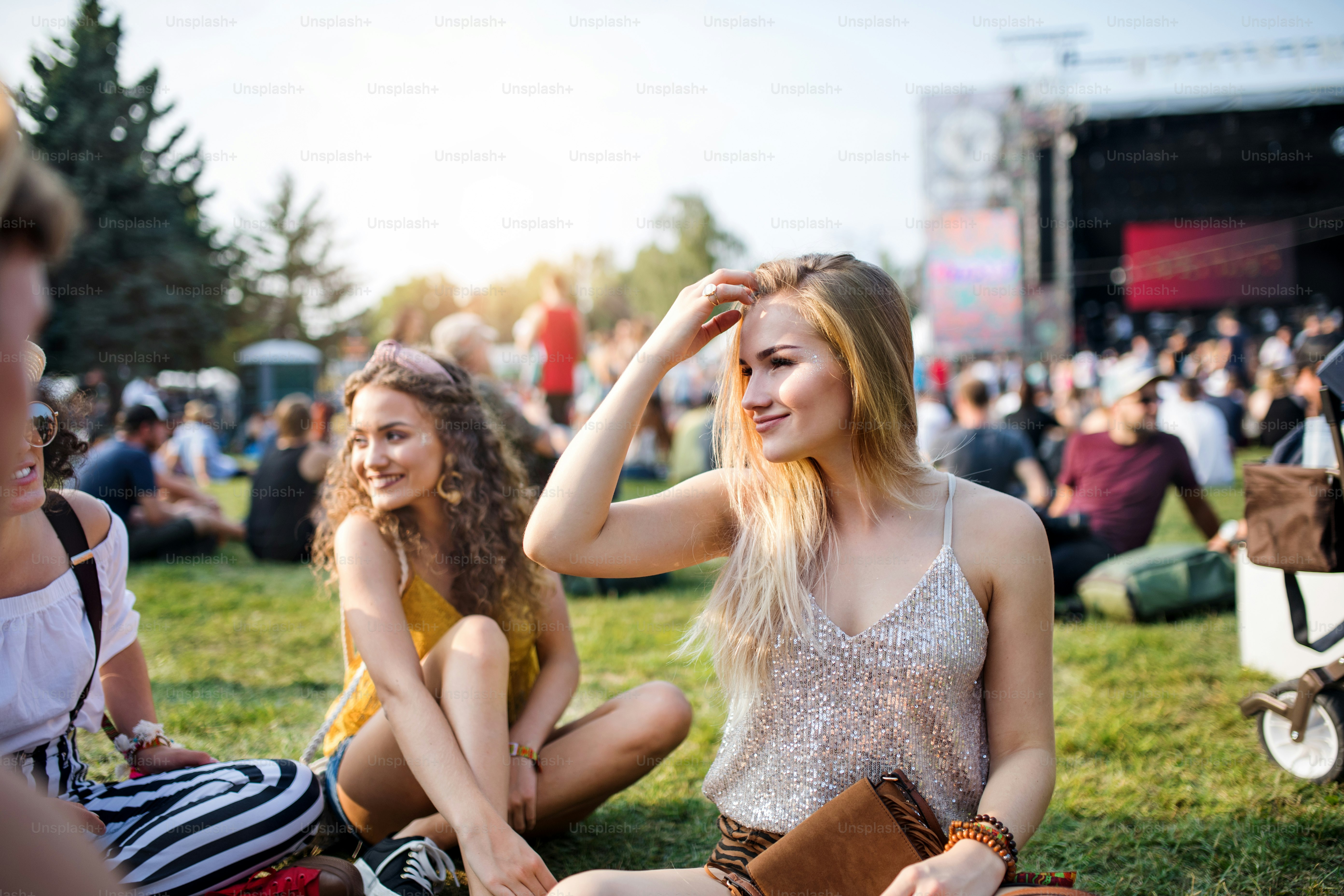Grupo de alegres amigas jóvenes sentadas en el suelo en el festival de verano, hablando.