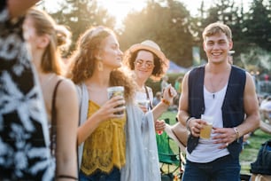 A group of young friends with drinks at summer festival, standing and talking.