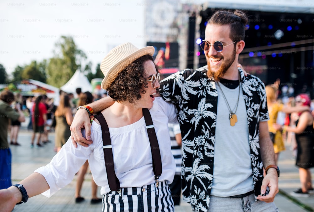 Portrait de face d’un jeune couple au festival d’été, marchant bras dessus, bras dessous.