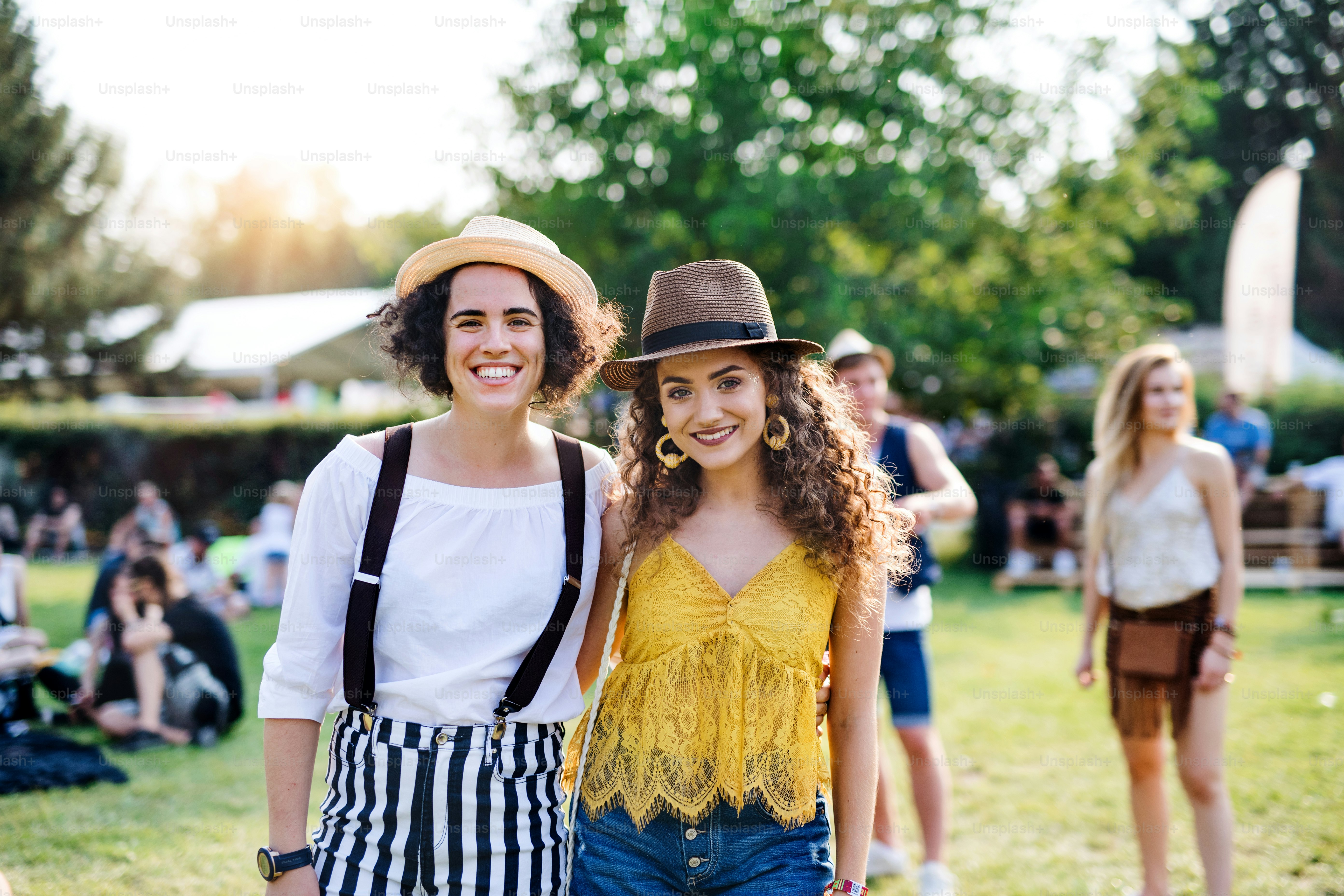 Portrait of two young women friends standing at summer festival, looking at camera.