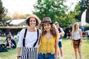 Portrait of two young women friends standing at summer festival, looking at camera.