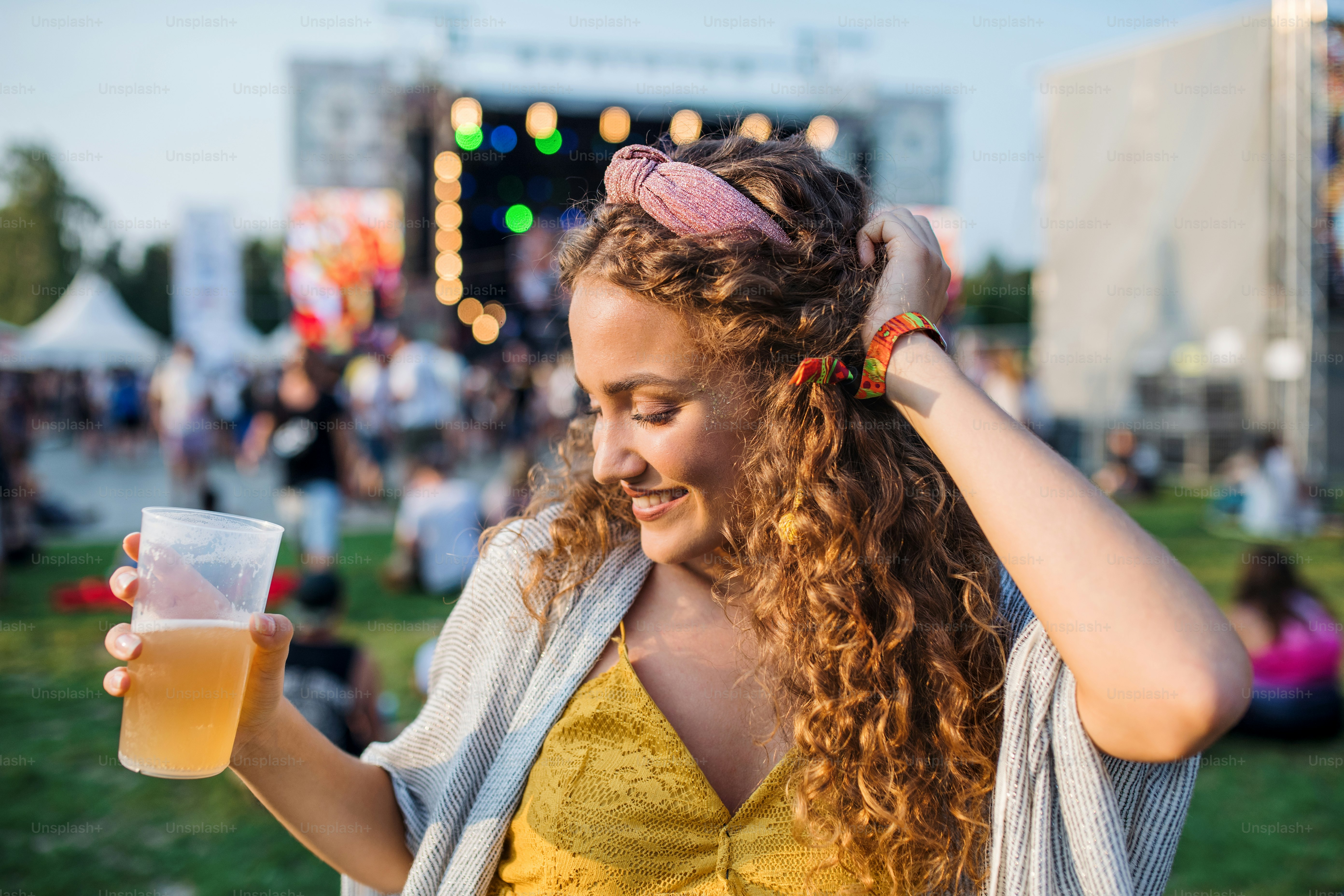 Una vista frontal de una mujer joven con bebida bailando en el festival de verano