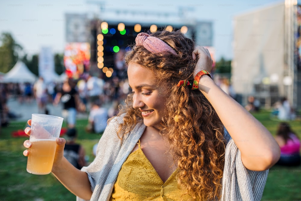 Uma vista frontal da jovem mulher com bebida dançando no festival de verão.