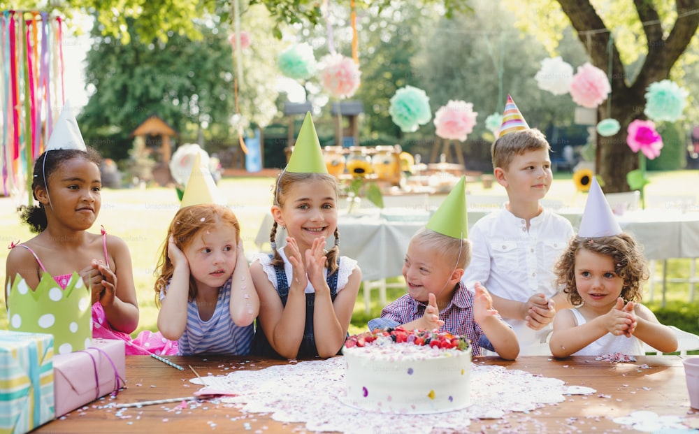 Down-Syndrom-Kind mit Freunden auf Geburtstagsfeier im Freien im Garten im Sommer.