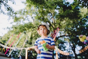 Low angle view of small boy standing outdoors on garden party, playing. Celebration concept.
