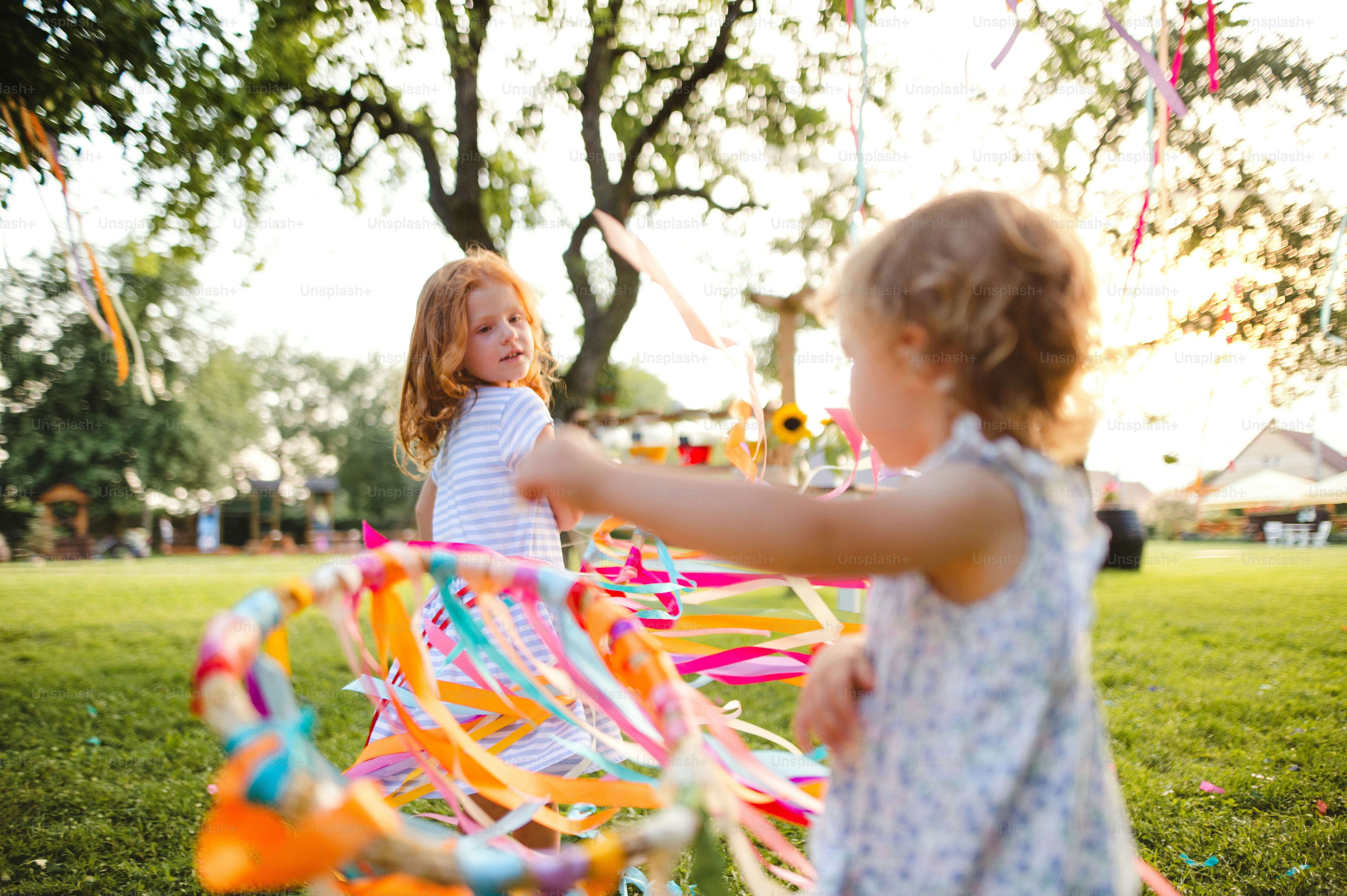 Small girls outdoors in garden in summer, playing with rainbow hand kite. A celebration concept