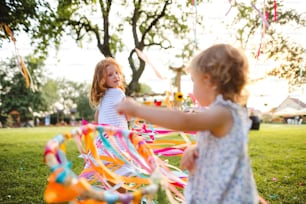 Kleine Mädchen draußen im Garten im Sommer, spielen mit Regenbogen-Handdrachen. Ein Festkonzept.
