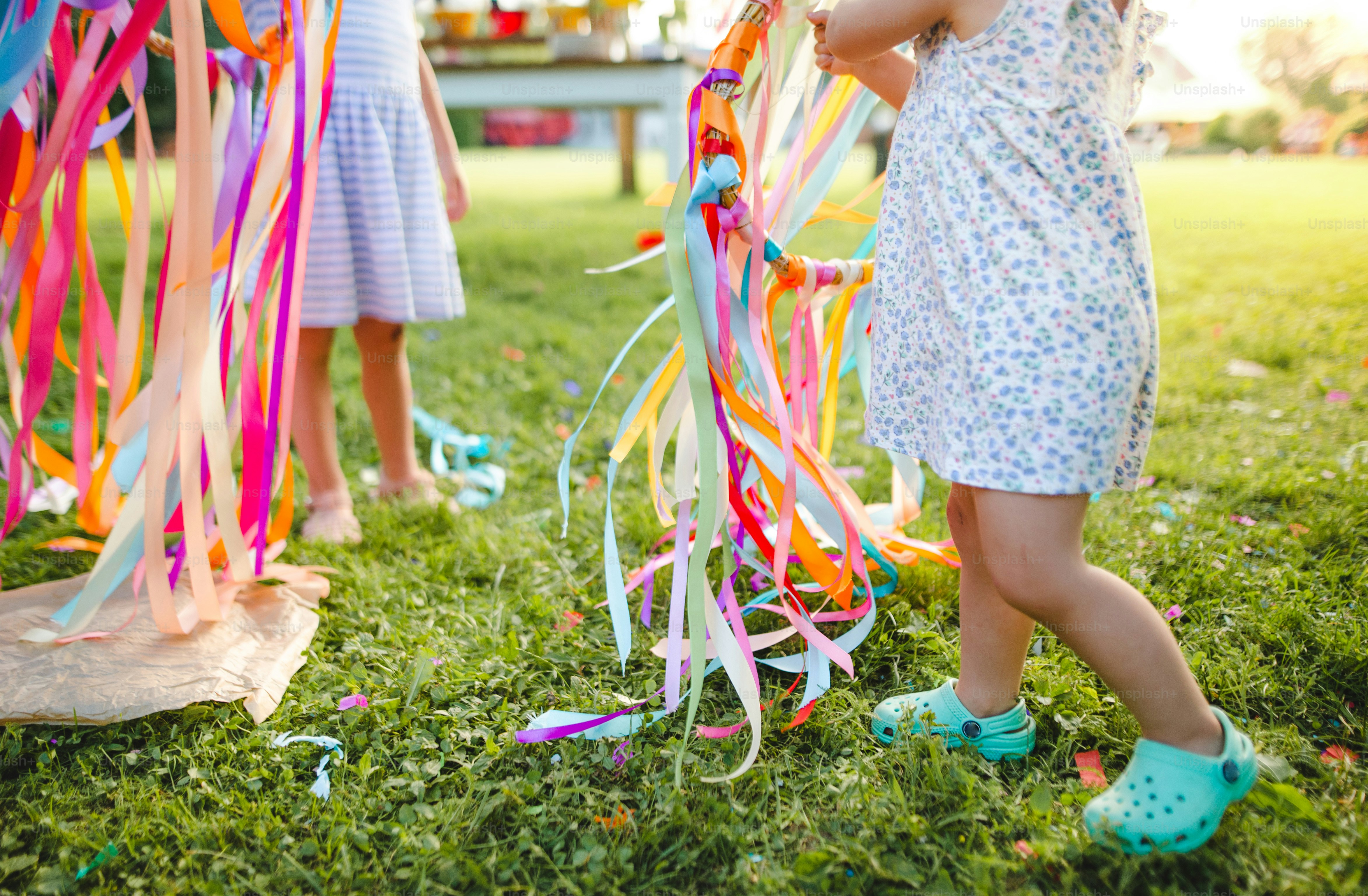 Gadis-gadis kecil yang tidak dapat dikenali di luar ruangan di taman di musim panas, bermain dengan layang-layang tangan pelangi. Konsep perayaan.