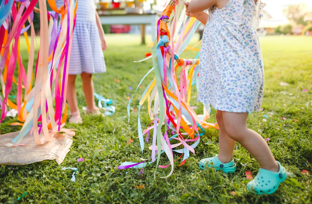Bambine irriconoscibili all'aperto in giardino in estate, giocando con l'aquilone arcobaleno. Un concetto di celebrazione.