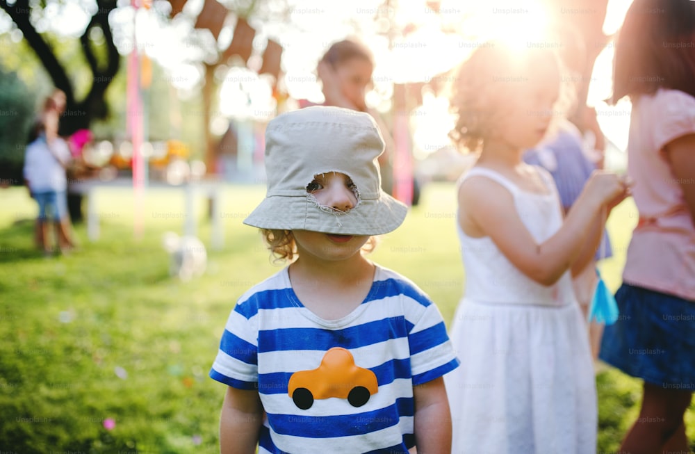 Small boy with friends standing outdoors on garden party in summer, hole in his hat. Celebration concept.