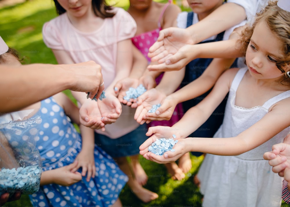 Unrecognizable small children outdoors in garden in summer, holding confetti. celebration concept.