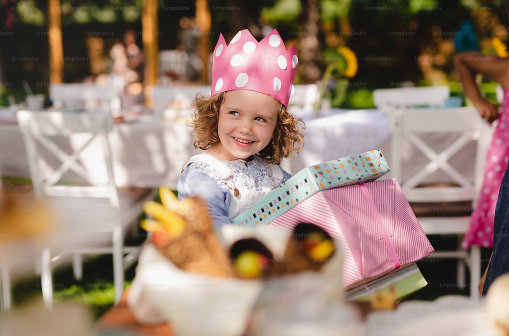Small girl with hat outdoors in garden in summer, holding presents. A celebration concept.