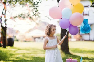 Petite fille dehors dans le jardin en été, jouant avec des ballons. Un concept de célébration.