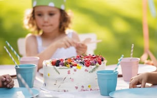 Vista frontal de niña pequeña con pastel celebrando cumpleaños al aire libre en jardín en verano, concepto de fiesta.